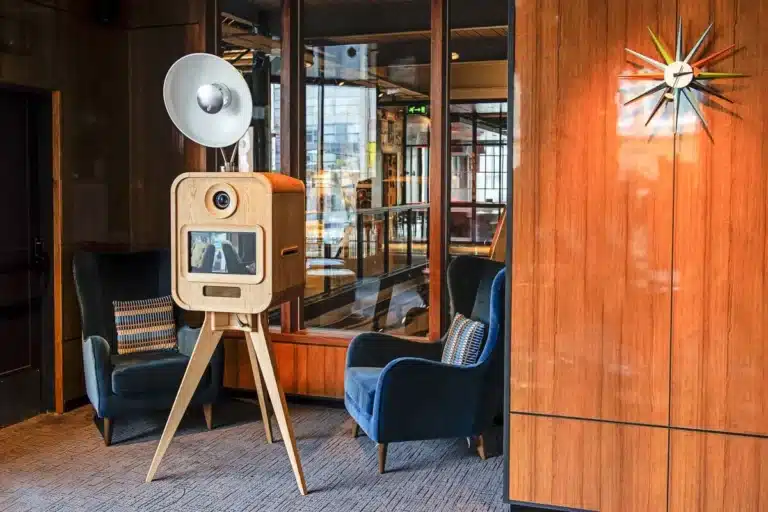 Luxury Oak photo booth with camera, screen and studio lighting beside blue armchairs.