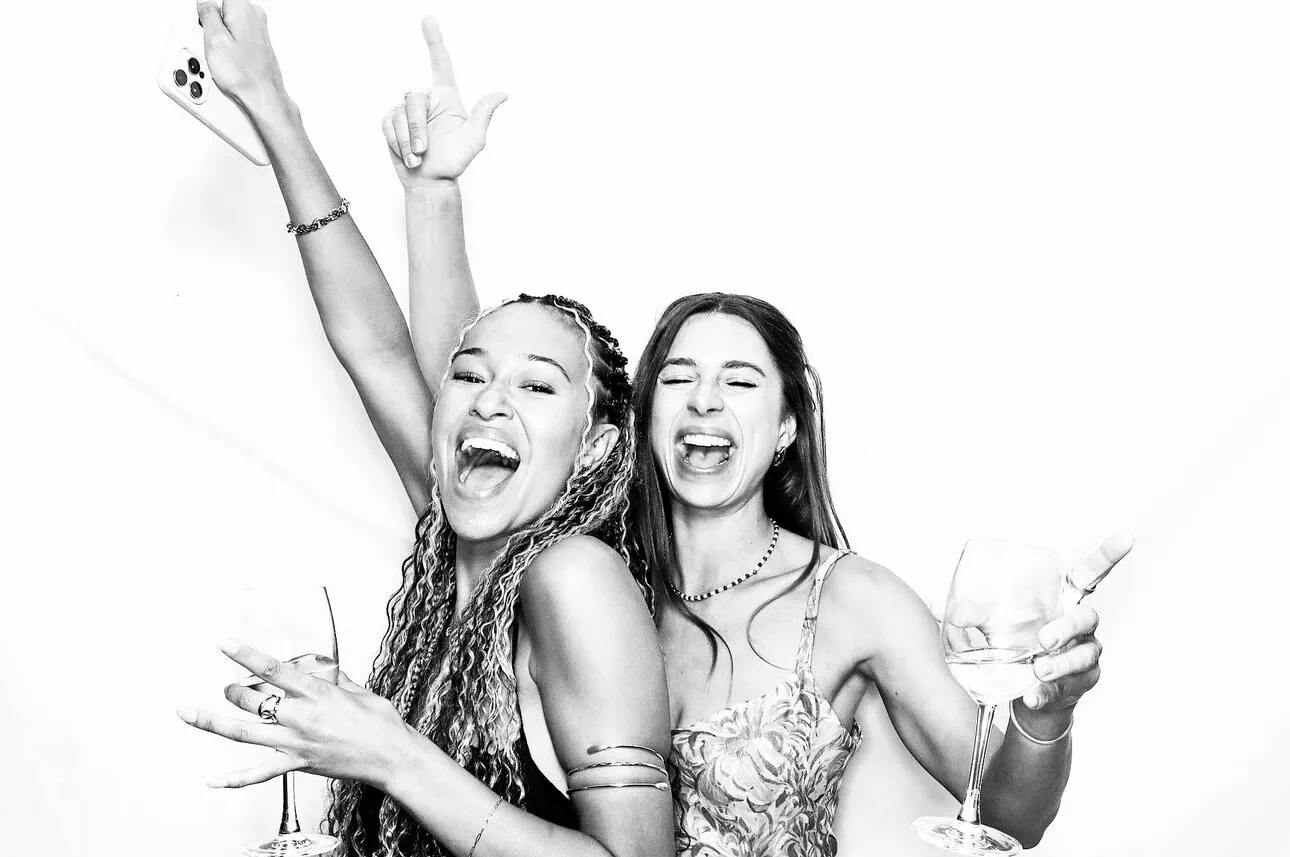 black and white photo of two female guests holding drinks and arm in the air