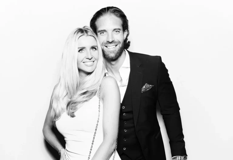 A man in a suit and a woman in a sleeveless dress stand close together, smiling at the camera against a plain white background, showcasing the fun of premium photo booth hire at a corporate event.
