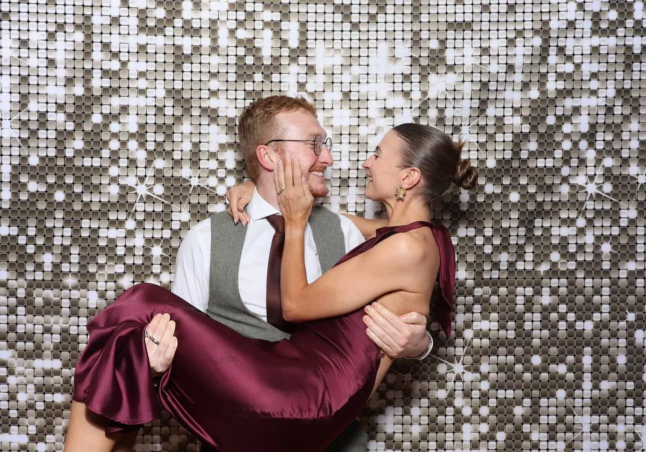 a gold shimmer wall backdrop with guests posing for the photo booth