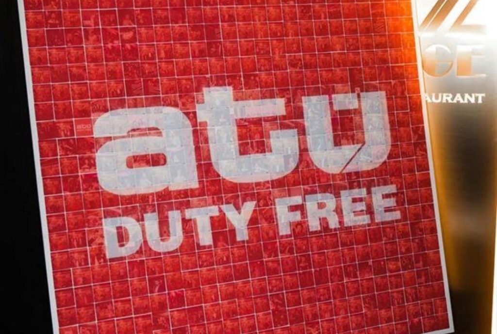 A sign with a red mosaic background displays the white text "atu DUTY FREE." Part of a gold and white sign, possibly related to premium photo booth hire, is visible on the right edge.