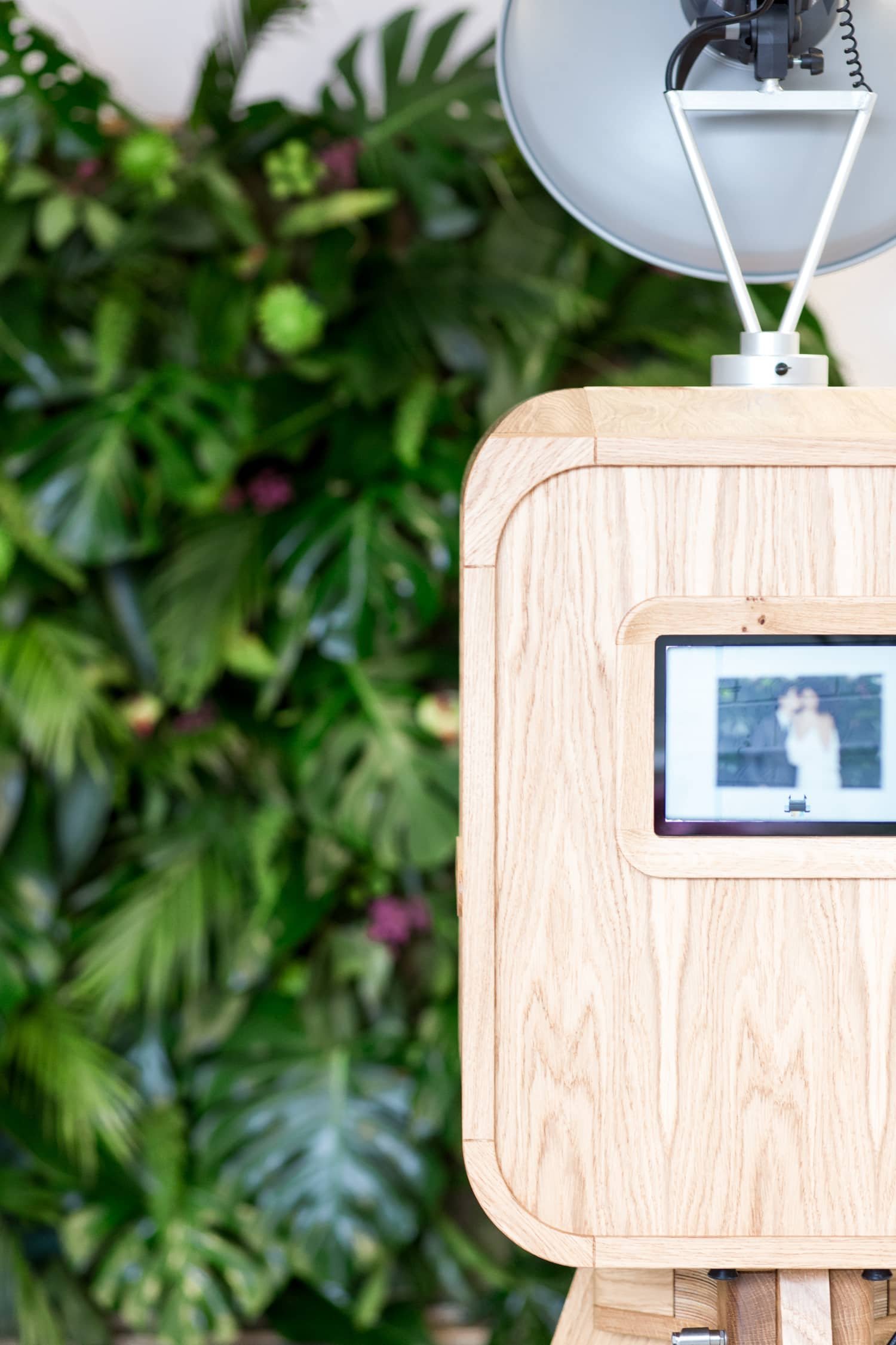 MooMuu Luxury Oak Booth beside a green foliage backdrop at an event.