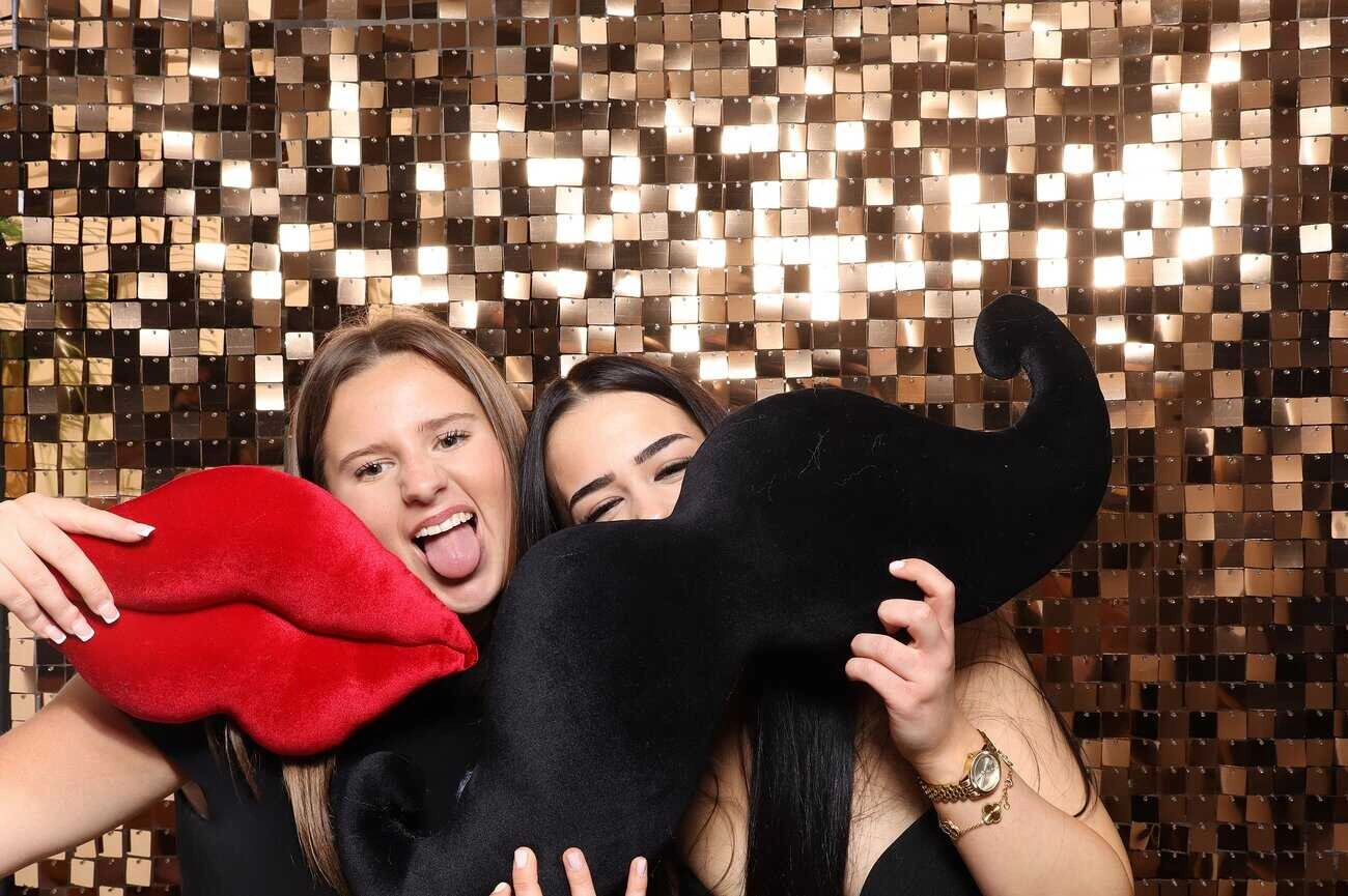 Two women holding a fake moustache and lips, adding a playful touch to celebrations.