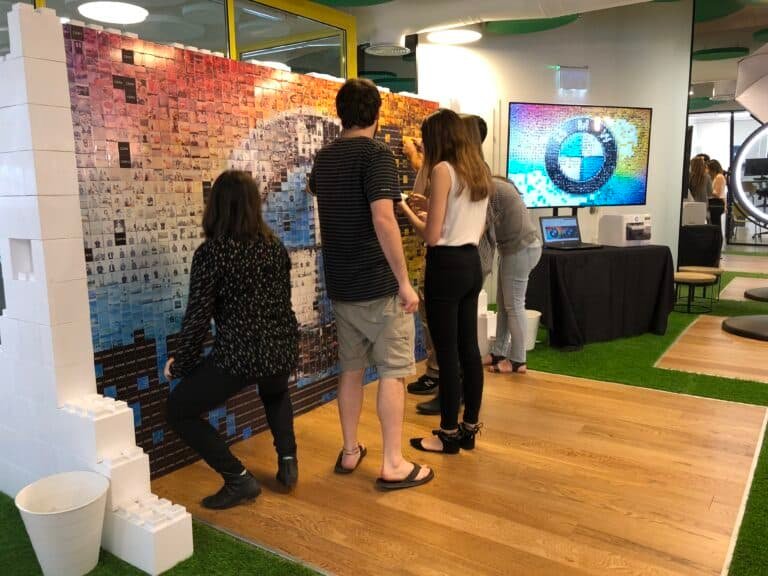 Guests adding photo tiles to a physical mosaic wall at a BMW event.