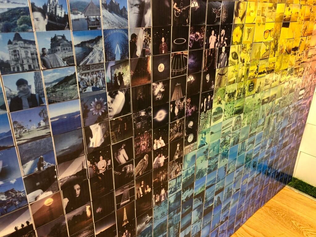 A wall covered with a mosaic of small, colourful photographs arranged in a gradient from blue to yellow, featuring landscapes, objects, and people—ideal for corporate event experiential setups or graffiti wall hire.