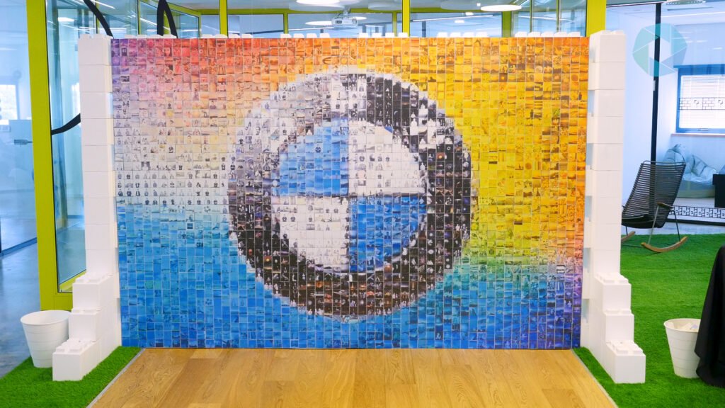 A mosaic wall featuring the BMW logo made up of many small individual photos, set indoors with glass walls, green artificial grass, and white decorative pillars—perfect for a corporate event experiential or sketch bot hire activation.