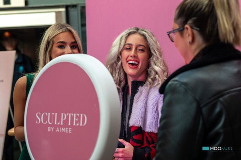 Guests smiling beside the Digital Booth with a pink Sculpted by Aimee branded rear panel.