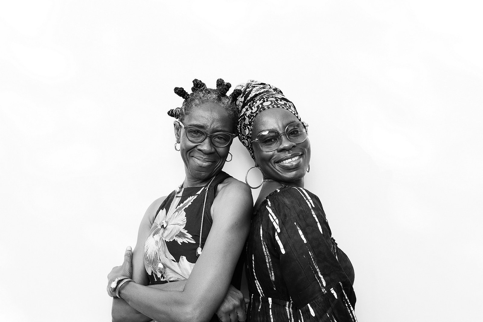 Two guests smiling back-to-back against a white backdrop in a Signature GLAM portrait.