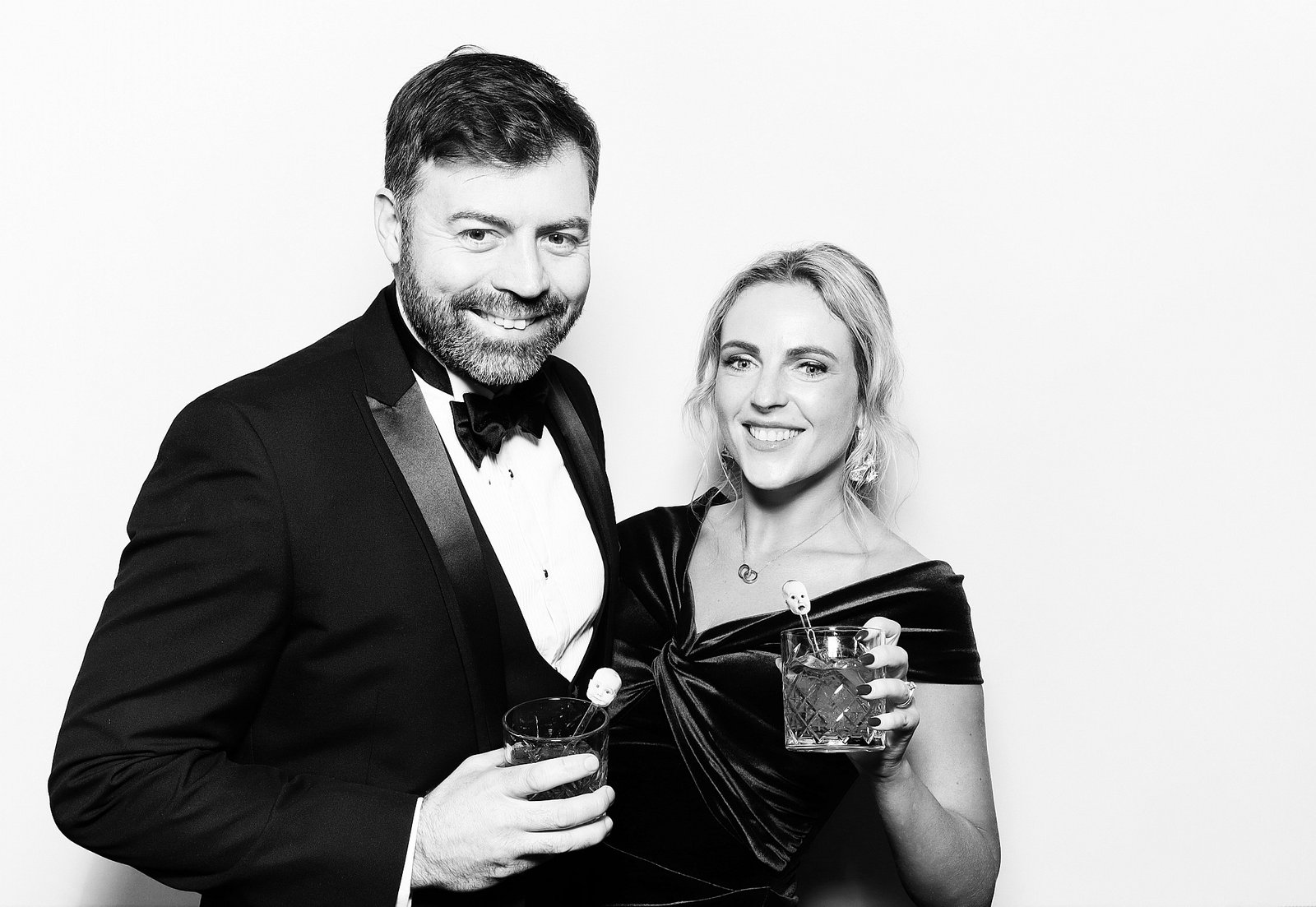 Two guests in black-tie eveningwear holding cocktails in a black-and-white Signature GLAM portrait.