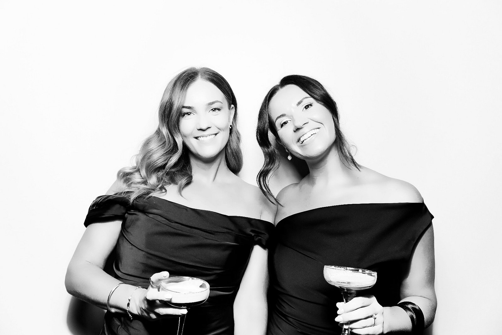 Two guests in evening dresses holding cocktails in a black-and-white Signature GLAM portrait.